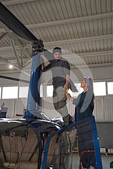 Handsome male and beautiful female working together with helicopter in garage