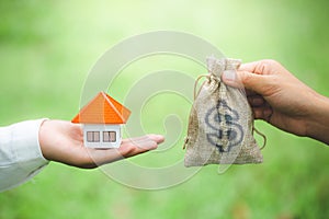 A man and a women hand holding a money bag and a model home Natural green background, Buying or selling a home, Loans for real