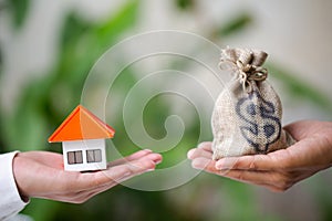 A man and a women hand holding a money bag and a model home Natural green background, Buying or selling a home, Loans for real