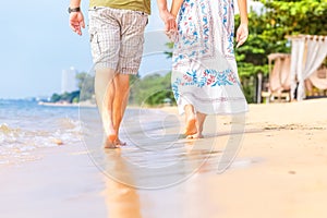 Man and women hold one`s hand on the  beach and front of sunset. they are couple. they are walking on the sand and water