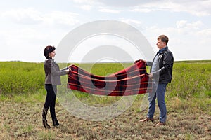 Man and woman lay a blanket on the ground for a picnic in nature