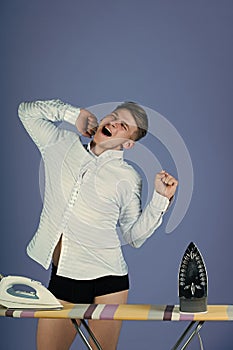 Man and women`s responsibilities. Tired man stretching and yawning at ironing board with irons