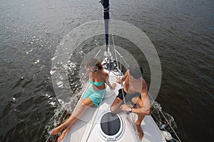 Man and woman sit on snout of yacht on river at photo