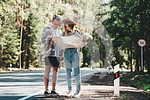 Man and woman traveling together and hold in hands location map and searching directional among trees in forest