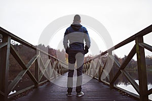 Man on wooden bridge over a lake, on a damp autumn day.