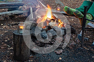 Man in the woods by the fire warms his feet in woolen socks, cropped photo, Camping concept, grill