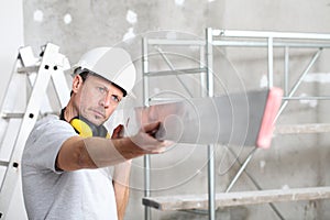 Man work,  checks the straightedge to level the wall, with ladder and scaffolding in the interior construction site on background