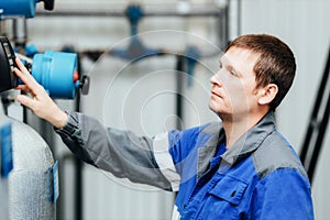 A man in work clothes checks the sensors of the boiler or compressor station. System monitoring.