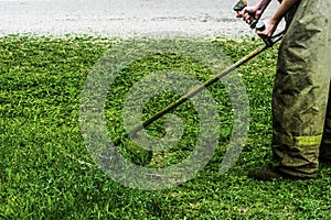 Man in work clothes mows green grass with a trimmer