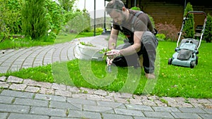 Man in work clothes pulls weeds on a beautiful lawn near a wooden house