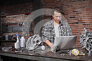 Man work with computer search in internet spare engine parts on the workbench in home garage workshop, diy concept