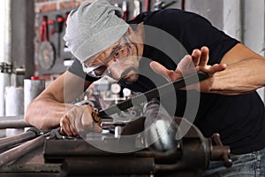 Man work with file rasp metal iron pipe gripped in vice on workbench table in garage workshop, do it yourself concept, hands close