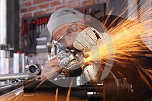 Man work in home workshop garage with angle grinder, goggles and construction gloves, sanding metal makes sparks closeup, diy and