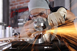 Man work in home workshop garage with angle grinder, goggles and construction gloves, sanding metal makes sparks closeup, diy and