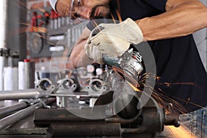 Man work in home workshop garage with angle grinder, goggles and construction gloves, sanding metal makes sparks closeup, diy and