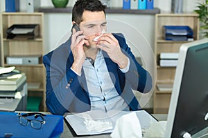 Man at work in office blowing nose with tissue