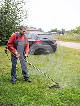 A man in work overalls mows grass on the lawn with a lawnmower. Taking care of the lawn with a lawnmower in summer on a