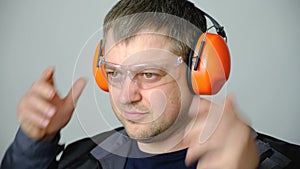 A man in work overalls puts on noise-canceling ear protectors, earmuffs on a white background.
