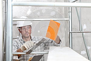 Man work, professional construction worker  with plastering tools on scaffolding, safety hard hat, gloves and protective glasses.