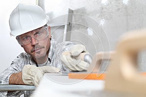 Man work, professional construction worker  with plastering tools on scaffolding, safety hard hat, gloves and protective glasses.