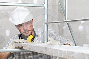 Man work, professional construction worker  with scaffolding, safety hard hat, hearing protection headphones, gloves and