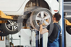 Man in work uniform changing car wheel indoors. Conception of automobile service