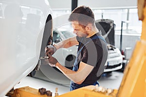 Man in work uniform repairs car indoors. Conception of automobile service