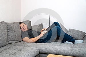 The man worked at home behind a laptop tired and sleeps on the couch