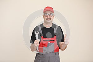 man worker in a black t shirt, glasses and red gray construction overall holds a new gray tool straight pipe wrench or