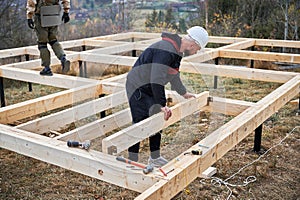 Man worker building wooden frame house on pile foundation.