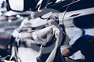 Man worker in car wash polishing car with cloth