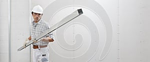 Man worker with drywall metal profile for installing plasterboard sheet to wall. Wearing white hardhat, work gloves and safety