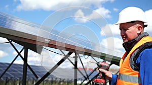 Man worker fixing solar panel to a metal basis with a drill. Solar power plant maintenance concept.