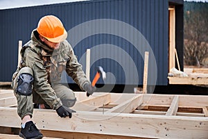 Man worker hammering while building wooden frame house.