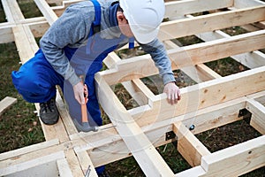 Man worker hammering while building wooden frame house.