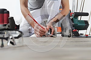 Man worker hands installing timber laminate floor, takes measurement with the tape measure and pencil. Wooden floors house renovat