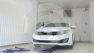 Man worker in mask during a pandemic washing white car on a car wash