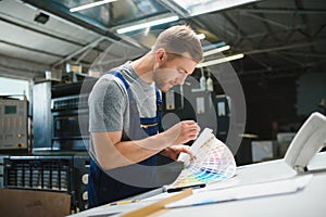 Man worker measuring printing color with spectrometer on the operating desk of the printing plant