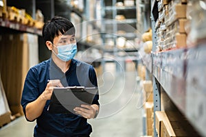 Man worker with medical mask holding clipboard and checking inventory in warehouse during coronavirus covid-19 pandemic