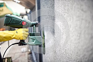 Man worker painting wall with grey paint using a professional spray gun. Man painting wall using protective gloves