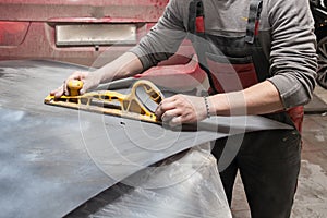 Man worker preparing for painting a car element using emery sender by a service technician leveling out before applying a primer