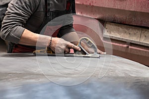 Man worker preparing for painting a car element using emery sender by a service technician leveling out before applying a primer