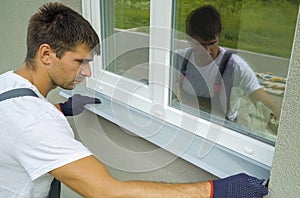 Man worker in protective gloves measuring external frame and PVC window metal sill size