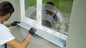 Man worker in protective gloves measuring external frame and PVC window metal sill size