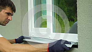 Man worker in protective gloves measuring external frame and PVC window metal sill size