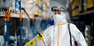 Man worker with protective mask and suit disinfecting industrial factory with spray gun.