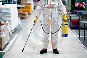 Man worker with protective mask and suit disinfecting industrial factory with spray gun.