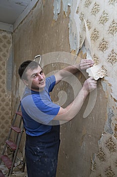 Man worker removing old wallpaper during overhaul