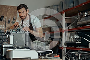 Man worker repair a coffee machine in own workshop and looking camera