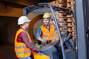 Man worker sitting in industrial forklift at warehouse talking to woman co-worker